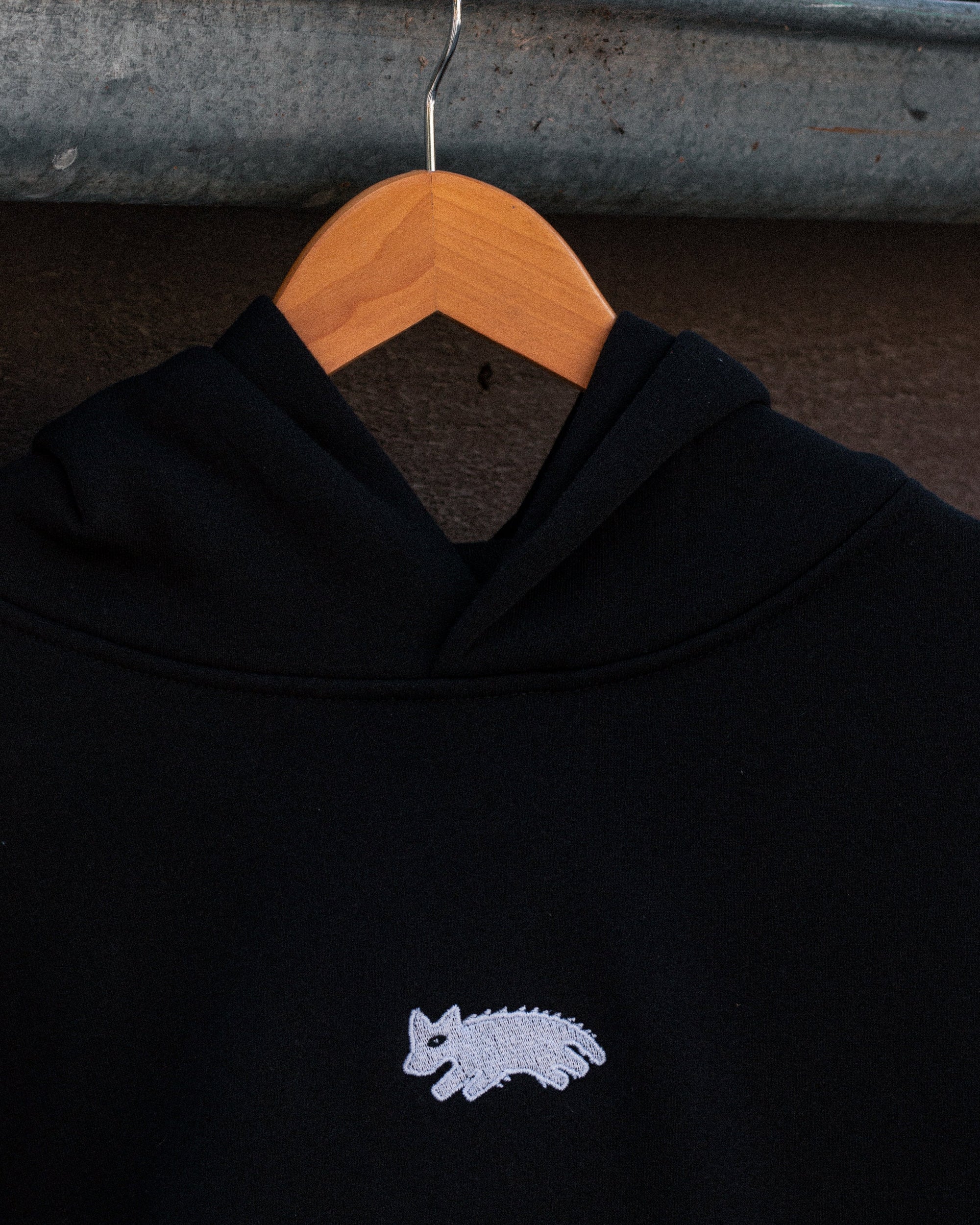 Black hoodie with a small logo on a wooden hanger against a dark background