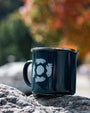 Navy mug with a white design on a rock with a blurred autumn background