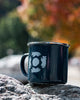 Navy mug with a white design on a rock with a blurred autumn background