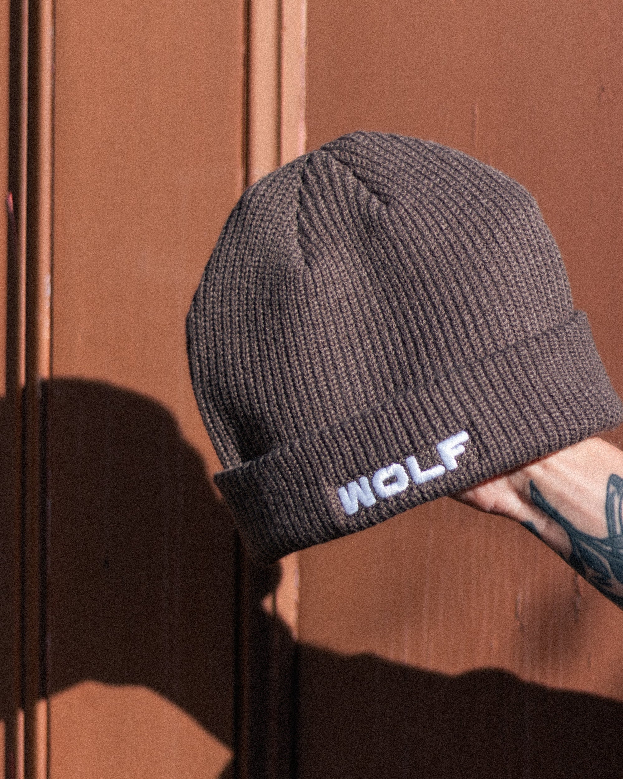 Beige beanie with 'WOLF' branding held against a brown background