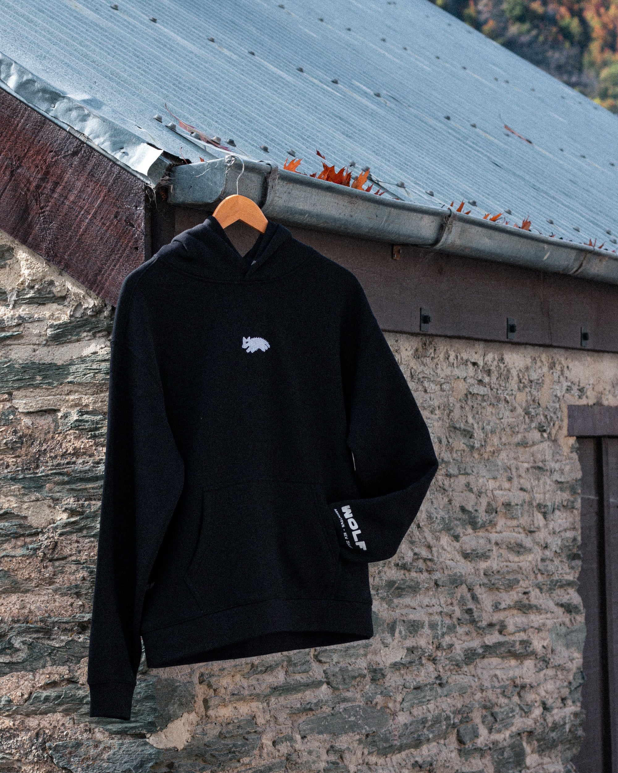 Black hoodie with a white logo on a hanger against a stone wall background