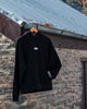 Black hoodie with a white logo on a hanger against a stone wall background