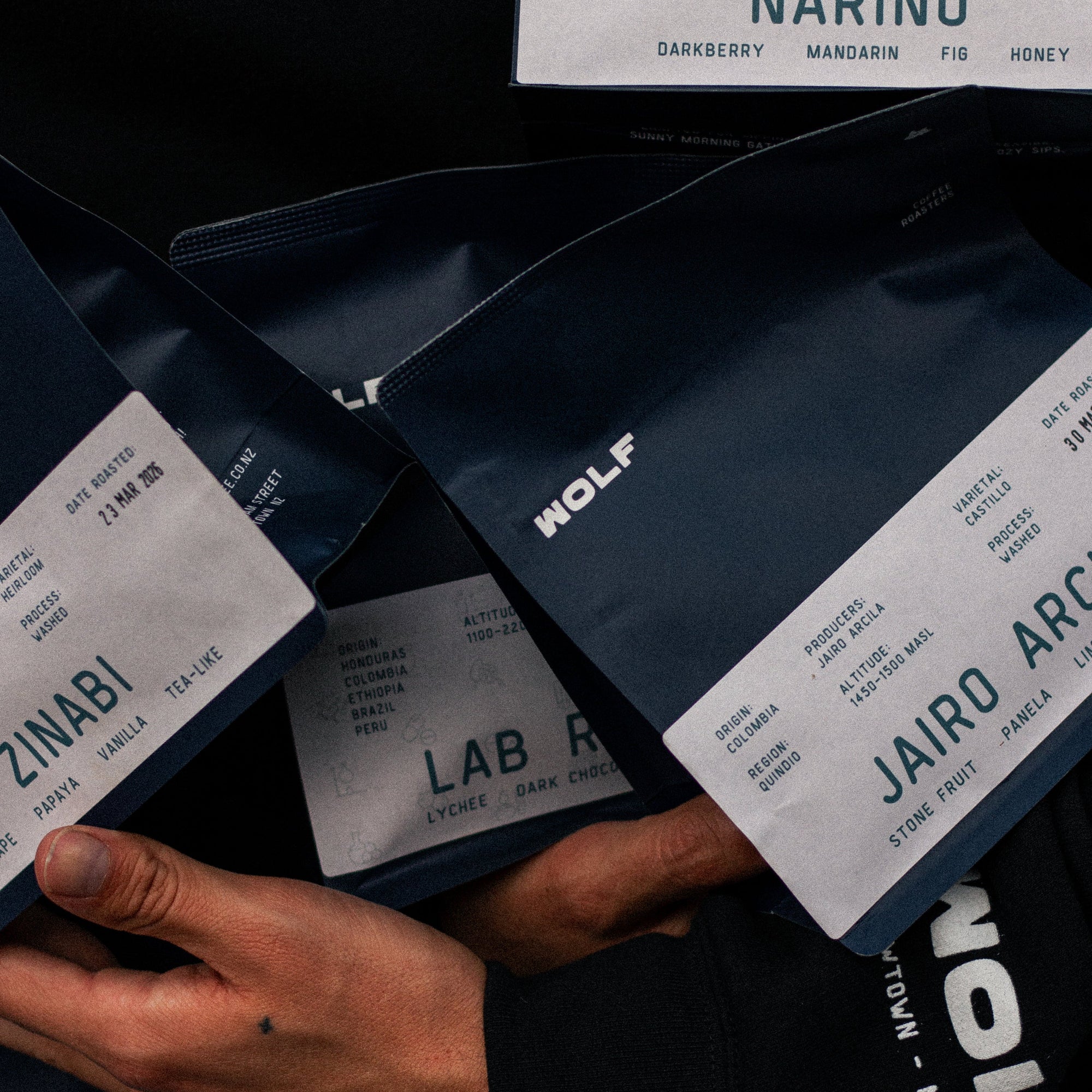 Multiple bags of coffee held by a person against a black hoodie.
