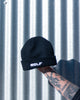 Black beanie with 'WOLF' branding held against a corrugated metal background
